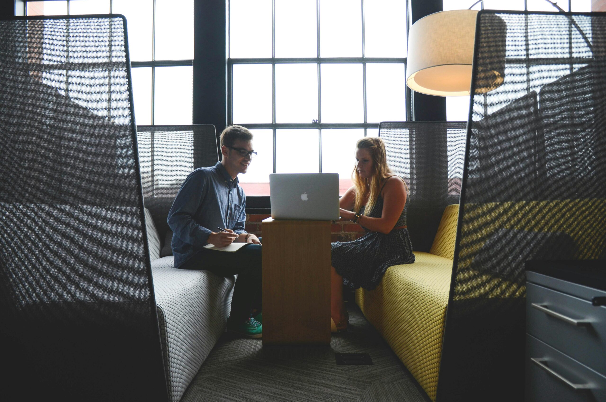 Two adults discussing work and collaborating in a modern office lounge area.